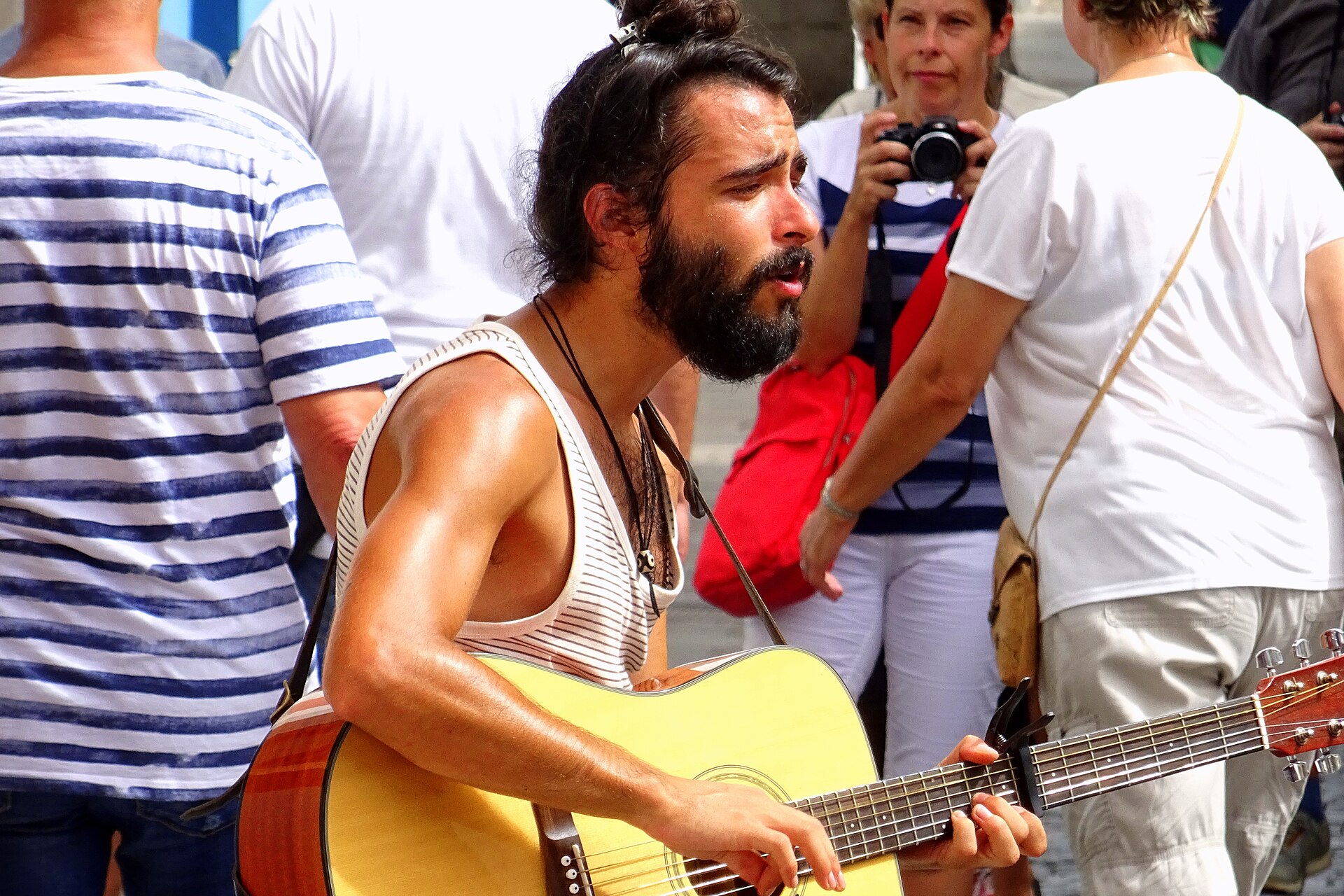 Straßenmusiker mit Gitarre singt bei der Fête de la Musique inmitten von Passant:innen, schwarz-weiß